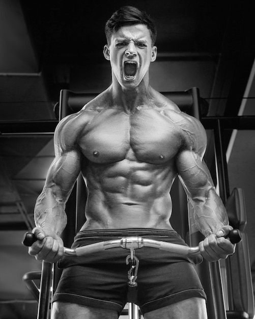 Jeune homme athlétique pompage des muscles dans la salle de gym à l'entraînement Sport et concept de soins de santé backgroun