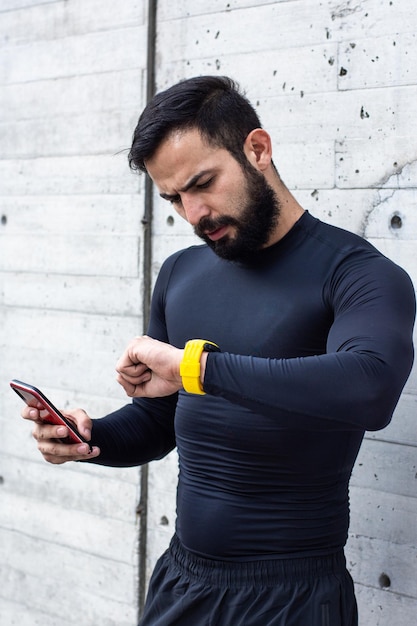 Jeune homme athlétique regarde sa montre à l'aide de son smartphone