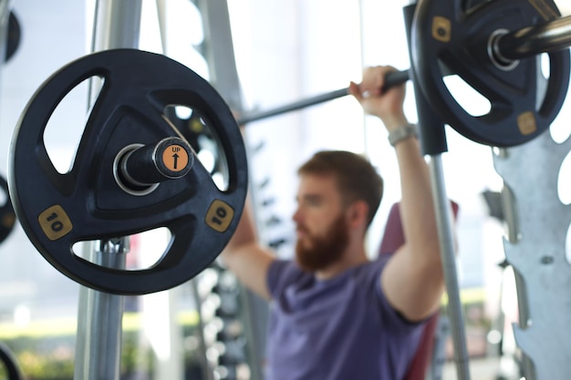 Jeune homme athlétique s'entraîne dans la salle de gym en faisant de l'exercice avec des haltères