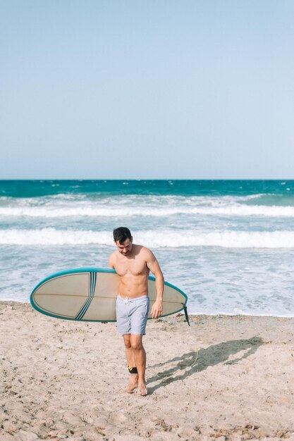 Jeune homme athlétique surfant sur la plage