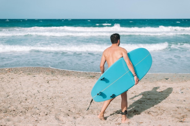 Jeune homme athlétique surfant sur la plage