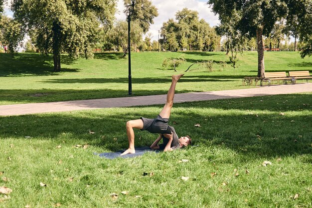 Jeune homme athlétique en tenue de sport, faire du yoga dans le parc