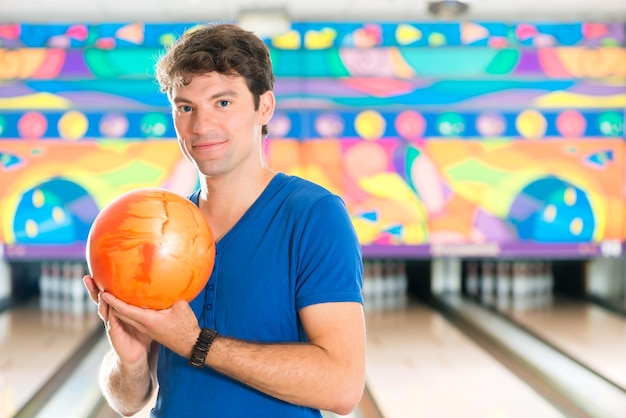 Jeune homme au bowling s'amusant, l'homme sportif tenant une boule de bowling en face de la ruelle à dix quilles