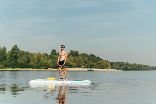 un jeune homme au corps athlétique se tient sur la rivière avec une rame dans les mains sur une planche à sup