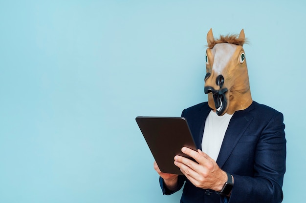 Jeune homme au masque de cheval drôle travaille avec une tablette portable.