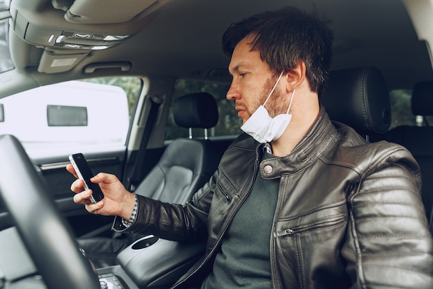 Jeune homme au masque médical à l'aide de smartphone en voiture