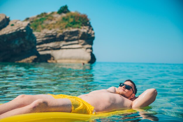 Jeune homme au matelas gonflable jaune dans de l'eau claire et transparente