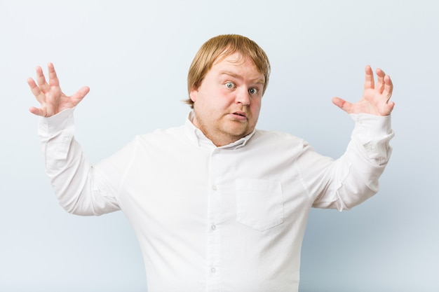 Jeune homme authentique, gros homme rousse, reçoit une agréable surprise, excité et levant les mains.