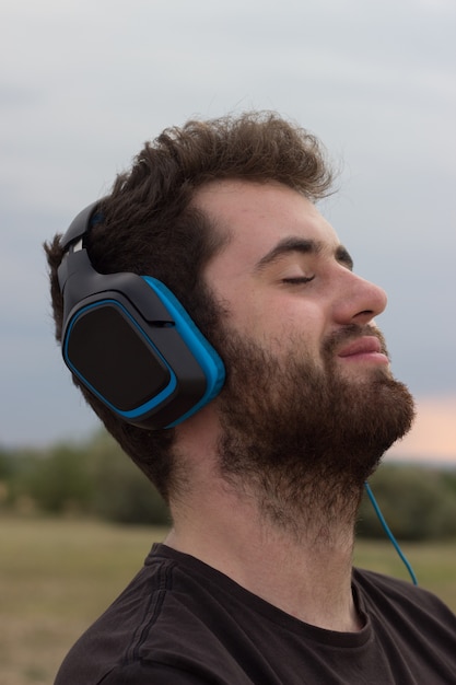 Jeune homme aux cheveux bouclés, écouter de la musique sur le terrain