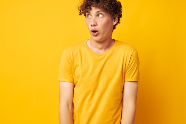 Jeune homme aux cheveux bouclés portant un t-shirt jaune élégant posant un style de vie inchangé