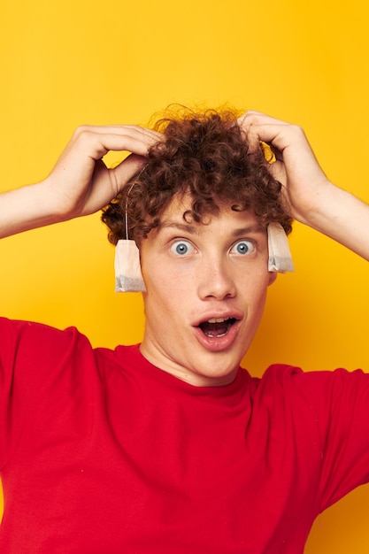 Jeune homme aux cheveux bouclés posant des sachets jetables de thé fond jaune inchangé