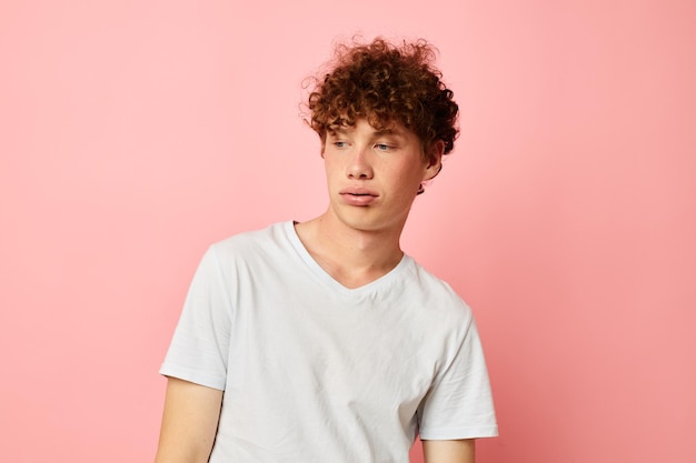 Jeune homme aux cheveux bouclés posant un t-shirt blanc de style jeunesse sur fond rose inchangé