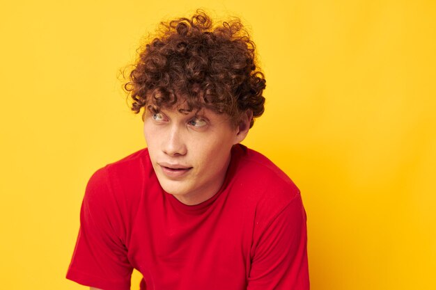 Jeune homme aux cheveux bouclés t-shirt rouge amusant posant des vêtements décontractés sur fond jaune inchangé