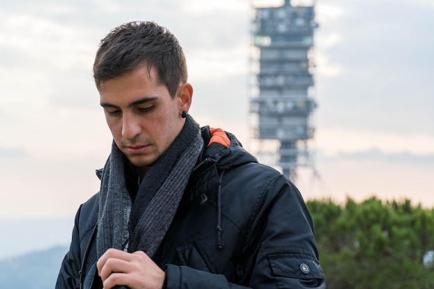 Un jeune homme aux cheveux bruns met son foulard en hiver et a l'air froid.