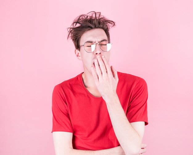 Jeune homme aux cheveux ébouriffés bâille de fatigue sur un fond rose. Concept de stress, de fatigue et de sommeil.