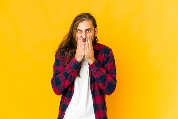 Jeune homme aux cheveux longs a l'air choqué, couvrant la bouche avec les mains