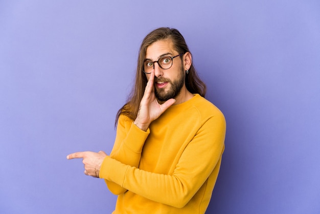 Un jeune homme aux cheveux longs a l'air de dire des ragots, en montrant le côté rapportant quelque chose.