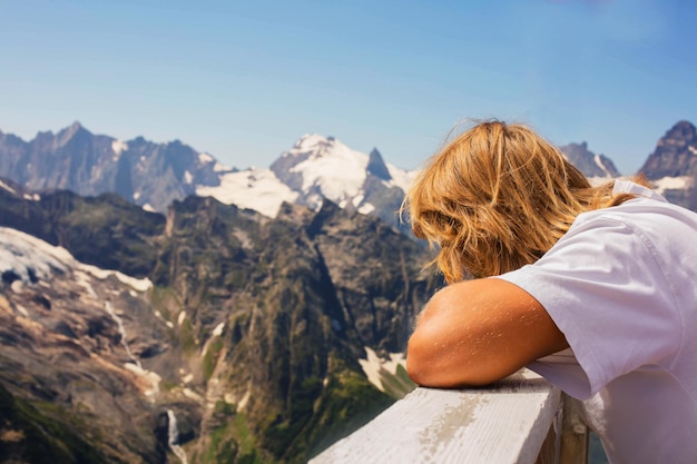 un jeune homme aux cheveux longs appuyé sur la balustrade admire les pentes enneigées des montagnes