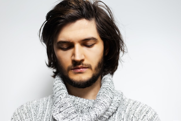 jeune homme aux cheveux longs sur un mur blanc.