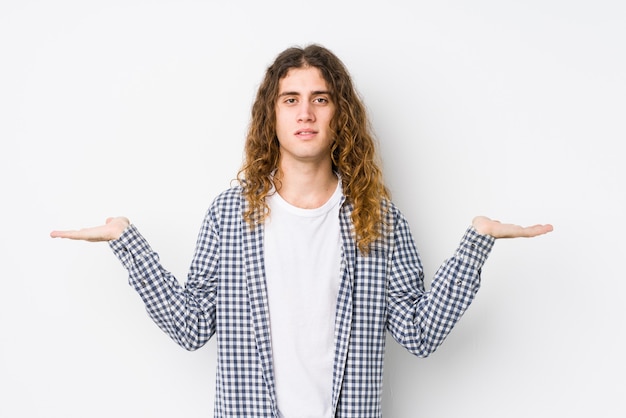 Jeune homme aux cheveux longs posant isolé fait échelle avec les bras, se sent heureux et confiant.