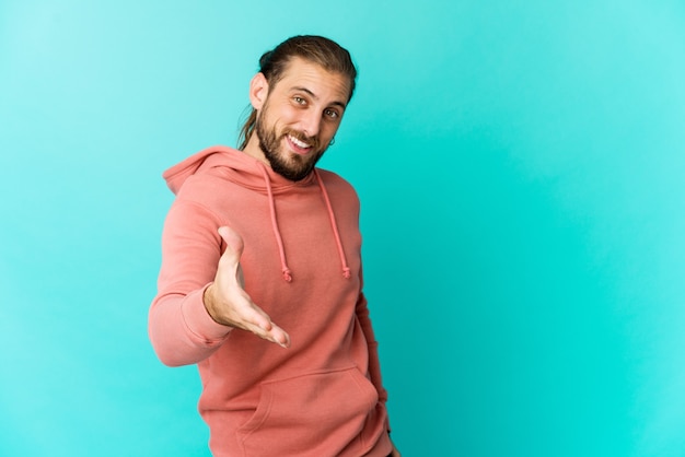 Jeune homme aux cheveux longs regarde étirement de la main en signe de salutation.