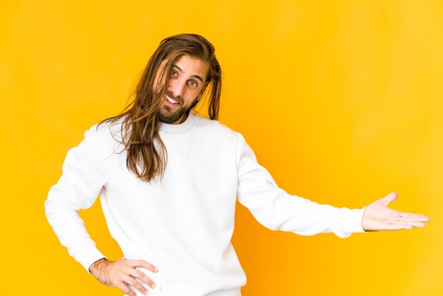 Jeune homme aux cheveux longs regarde montrant une expression bienvenue