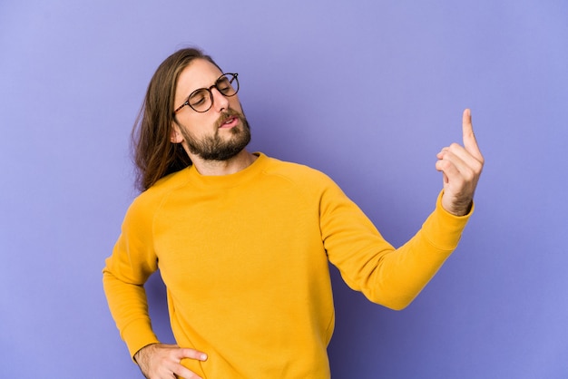 Jeune homme aux cheveux longs regarde pointé du doigt vers vous comme s'il vous invitait à vous rapprocher.