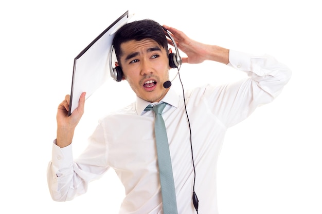 Jeune homme aux cheveux noirs en chemise blanche avec cravate bleue et casque tenant un dossier sur fond blanc en studio