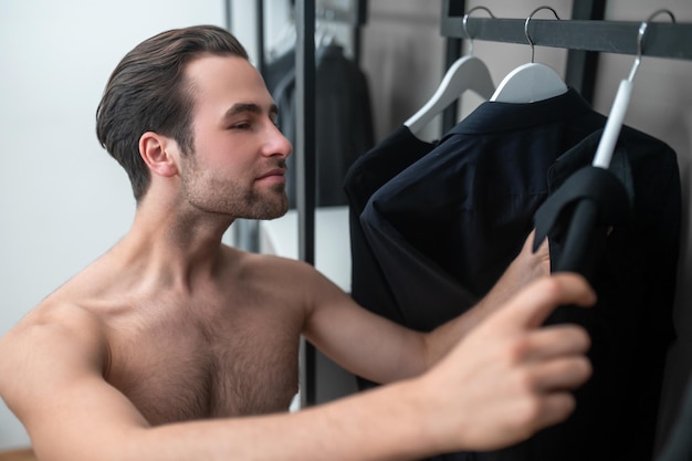 Jeune homme aux cheveux noirs choisissant des vêtements dans sa garde-robe