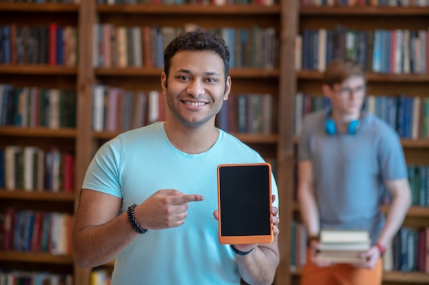 Jeune homme aux cheveux noirs dans un t-shirt bleu montrant sa tablette