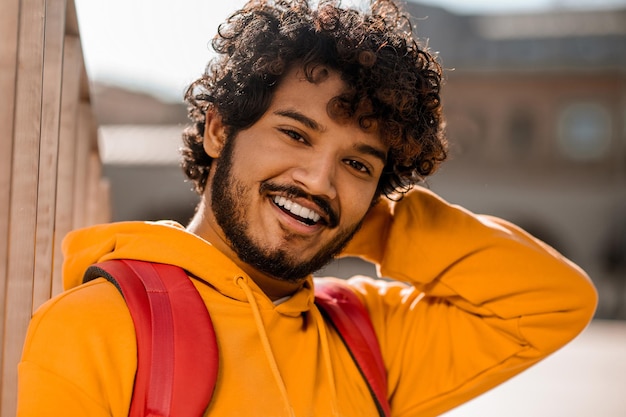 Jeune homme aux cheveux noirs en sweat à capuche orange avec un sac à dos