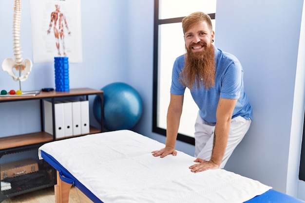 Photo un jeune homme aux cheveux roux portant l'uniforme d'un physiothérapeute se tient dans une clinique de physiothérapie