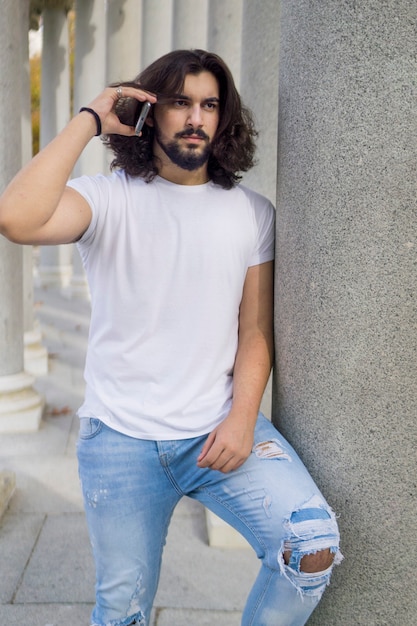 Photo jeune homme aux longs cheveux flottants s'appuyant sur une colonne parlant au téléphone