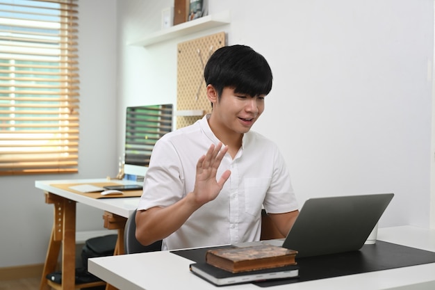 Jeune homme ayant un appel vidéo sur un ordinateur portable alors qu'il était assis au bureau à domicile.