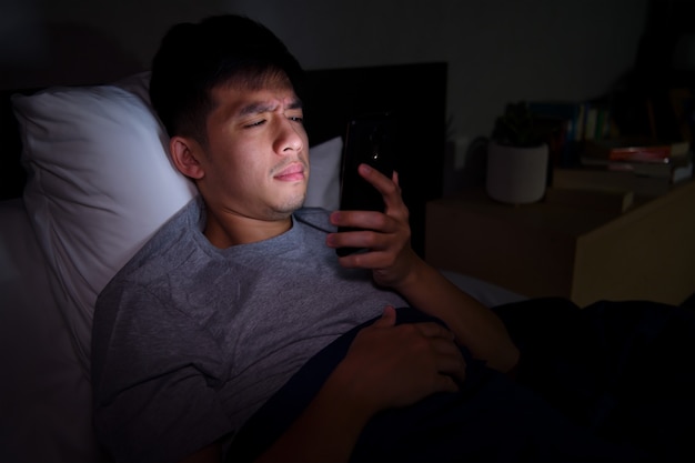 Jeune Homme Ayant Les Yeux Endoloris Et Fatigués Lors De L'utilisation De Smartphone En Position Couchée Dans Son Lit La Nuit