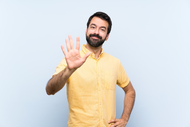 Jeune homme à la barbe sur bleu isolé comptant cinq avec les doigts