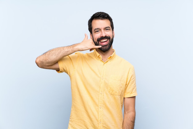 Jeune homme à la barbe sur bleu isolé faisant un geste de téléphone. Rappelle-moi