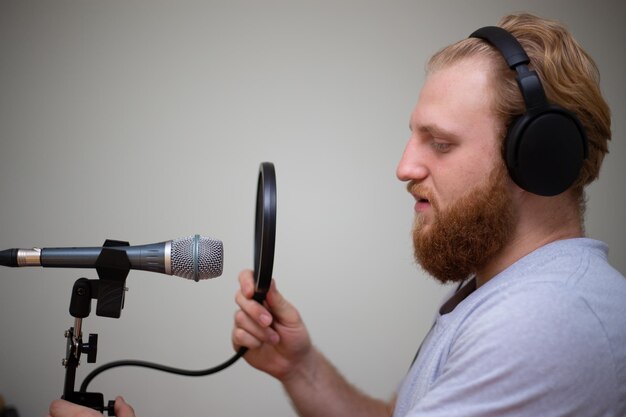 Un jeune homme avec une barbe chante dans un microphone de studio avec un filtre anti-pop