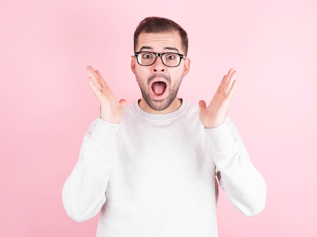 Jeune homme avec barbe et lunettes portant un pull décontracté sur fond rose