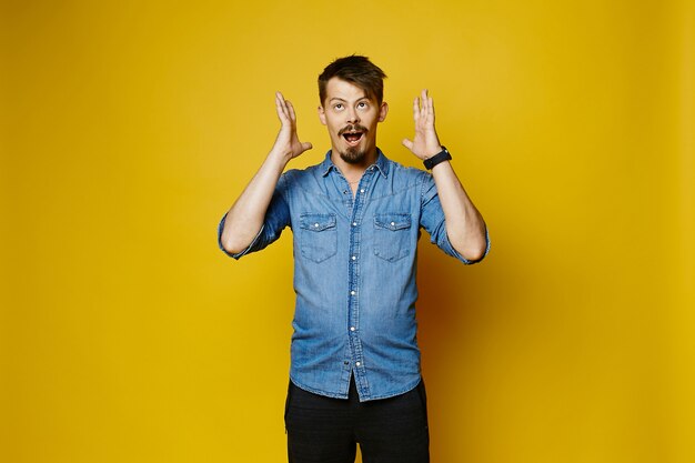 Jeune homme avec barbe et moustache pointant le doigt et regardant dans la caméra, isolé sur fond jaune. Jeune hipster émotionnel