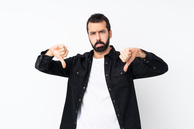 Jeune homme à la barbe sur mur blanc isolé, montrant le pouce vers le bas