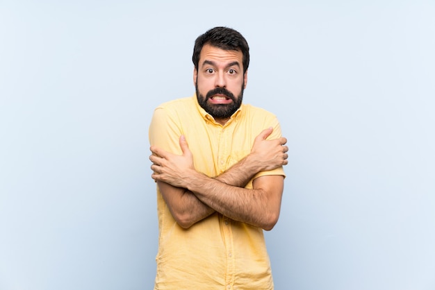 Jeune homme à la barbe sur mur bleu isolé gelant