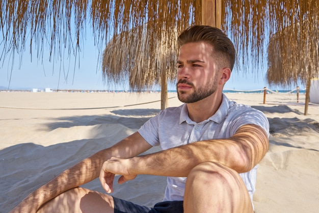 jeune homme barbe sur une plage sous un parasol