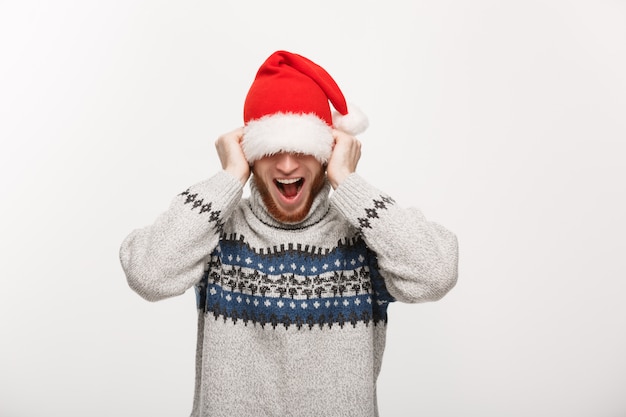 Jeune homme barbe en pull aime jouer avec le bonnet de Noel.