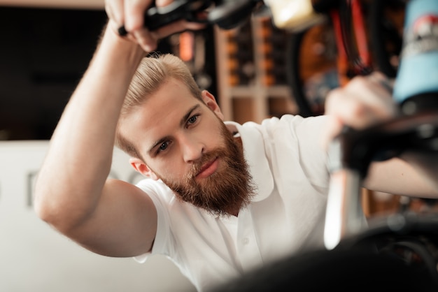 Un jeune homme avec une barbe regarde les détails de la bicyclette