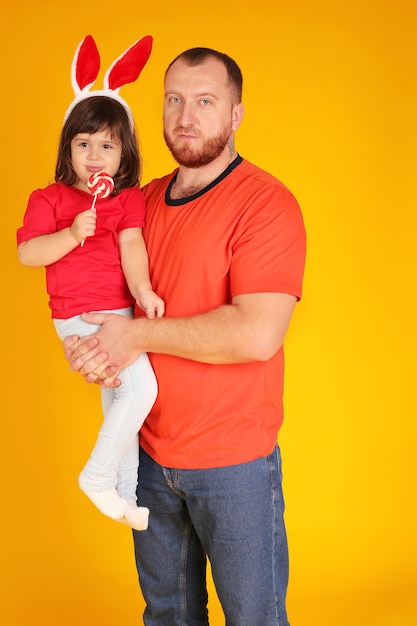 un jeune homme à la barbe rousse tient dans ses bras une petite fille avec des oreilles de lapin sur la tête