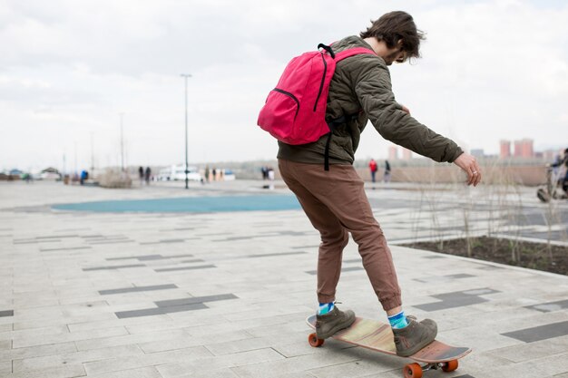 Jeune homme avec une barbe avec un sac à dos et un longboard dans la rue