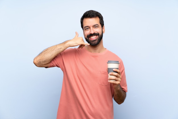 Jeune homme à la barbe tenant un café à emporter au cours de geste de téléphone bleu isolé