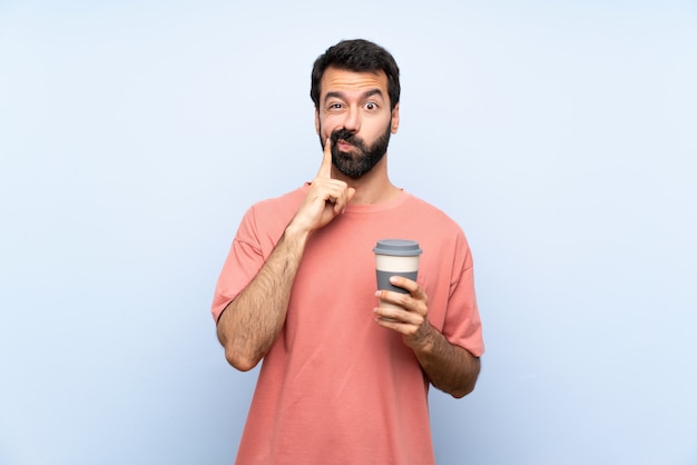 Jeune homme à la barbe tenant un café à emporter sur un mur bleu isolé