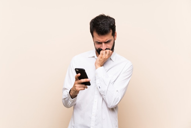 Jeune homme à la barbe tenant un mobile ayant des doutes